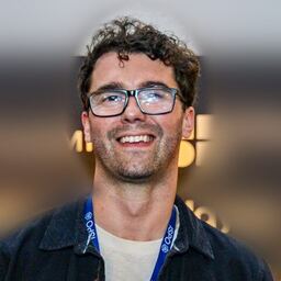 Dean Lynn, smiling, wearing glasses and a dark jacket