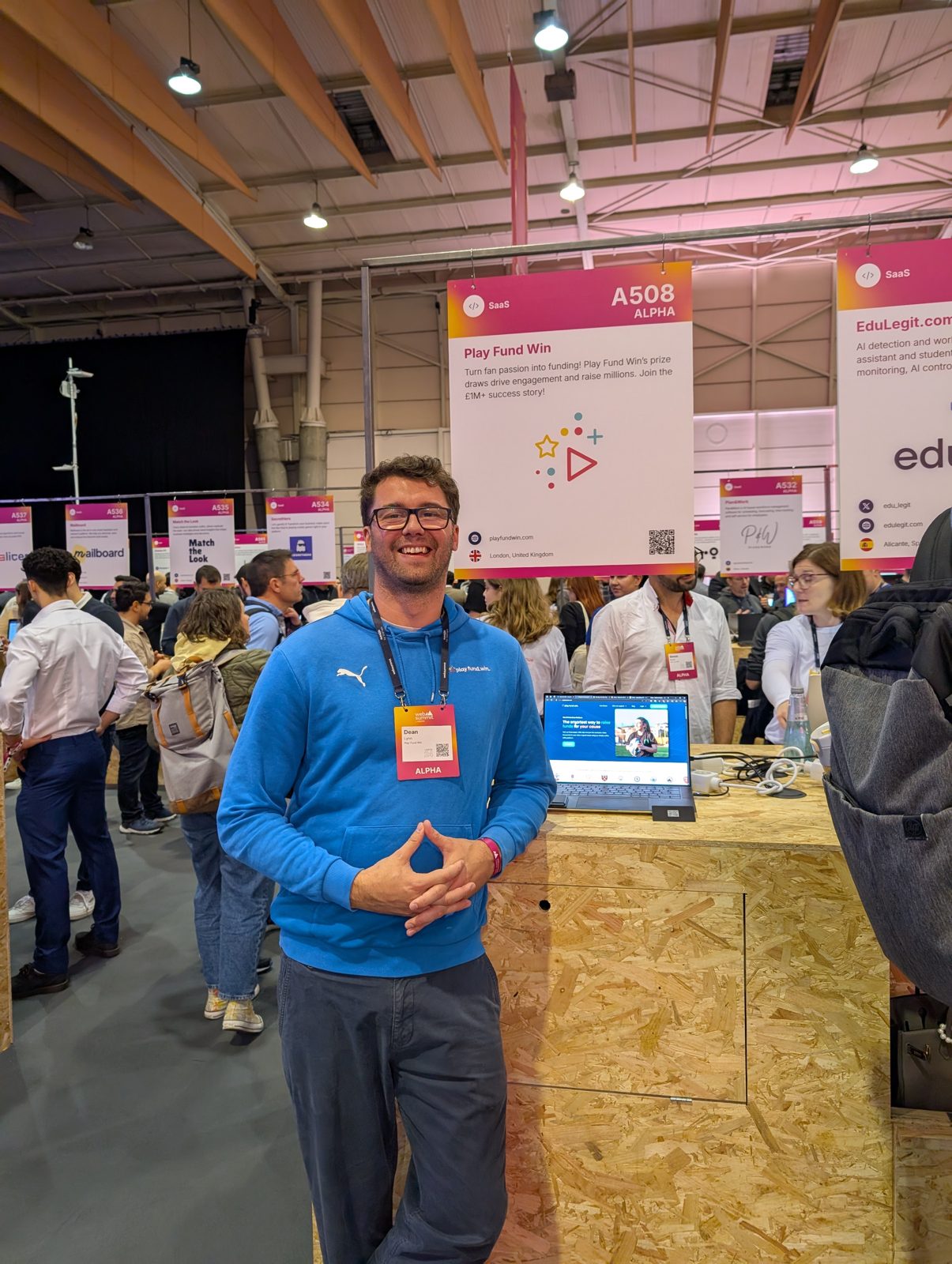 Standing at the Play Fund Win stand, A508 Alpha, on the Web Summit exhibition floor, a laptop on the counter beside him